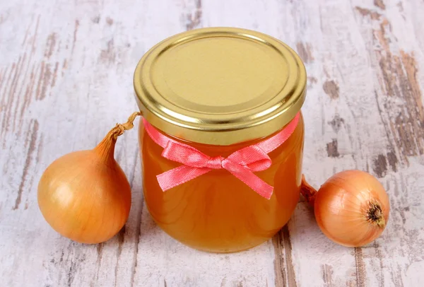 Fresh organic honey in glass jar and onions on wooden background, healthy nutrition and strengthening immunity