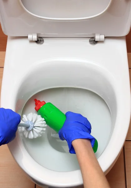 Hand of woman in blue glove cleaning toilet bowl