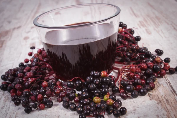 Bunch of fresh elderberry with juice on old wooden background, healthy nutrition