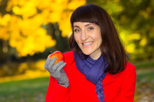 Happy woman with fresh apple in autumnal park, autumn concept