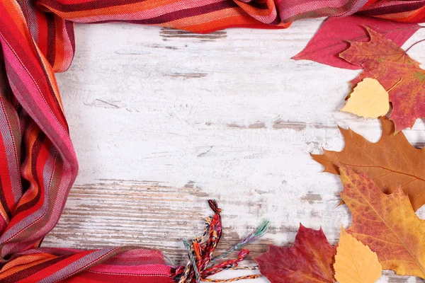 Womanly woolen shawl and autumnal leaves with copy space for text, old rustic wooden background