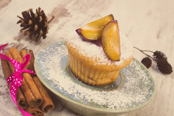 Vintage photo, Muffins with plums and powdered sugar, cinnamon sticks on old wooden background, delicious dessert