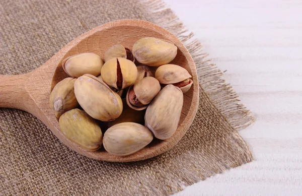 Pistachio nuts with spoon on white wooden table, healthy eating