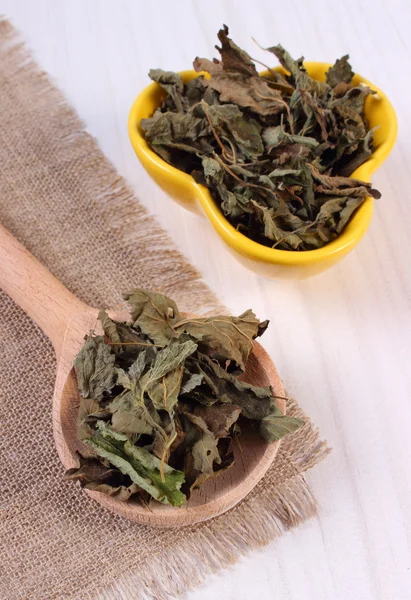 Dried lemon balm with spoon and bowl on wooden table, herbalism