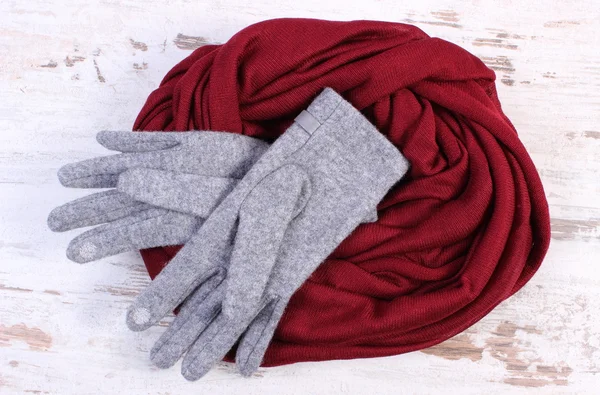 Pair of woolen gloves and shawl for woman on old wooden background