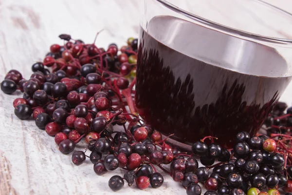 Bunch of fresh elderberry with juice on old wooden background, healthy nutrition