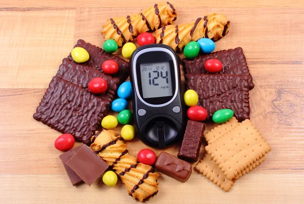 Glucometer with heap of sweets on wooden surface, diabetes and unhealthy food