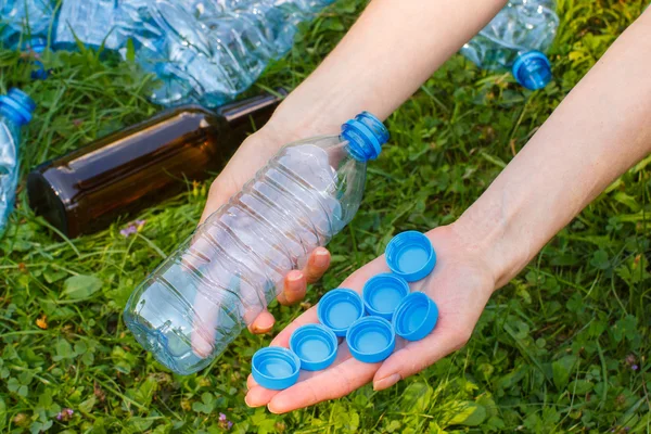 Hand of woman with plastic bottle and bottle caps, littering of environment