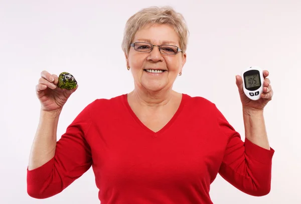 Happy senior woman holding glucometer and fresh cupcake, measuring and checking sugar level, concept of diabetes