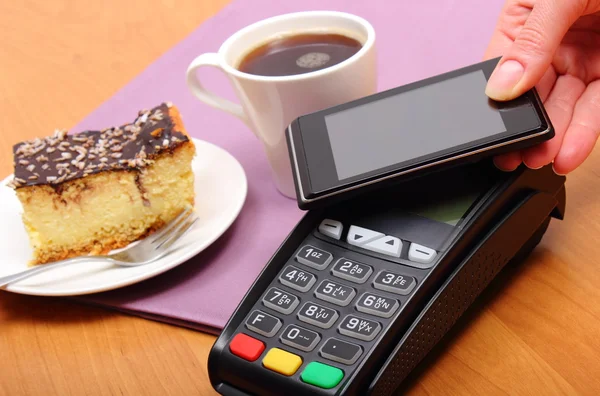 Paying with mobile phone with NFC technology for cheesecake and coffee in cafe, finance concept