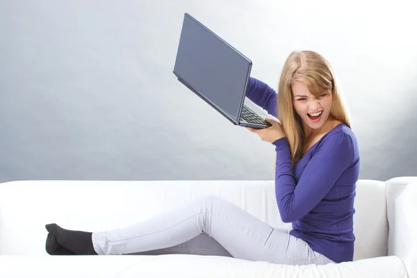 Angry woman sitting on sofa and throwing laptop, computer problem