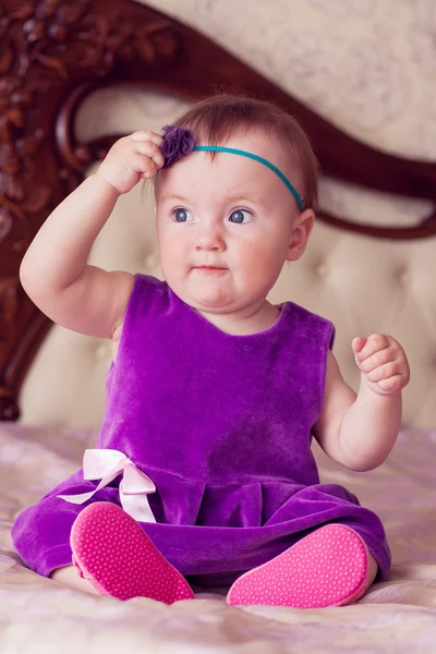 Baby in violet dress touching her headband and looking left