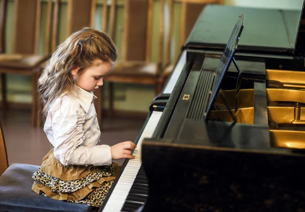 Cute little girl playing grand piano in music school