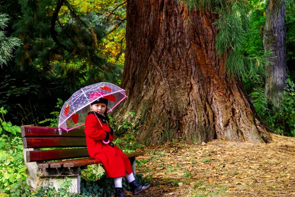 Cute little girl with umbrella sitting under the big pinetree