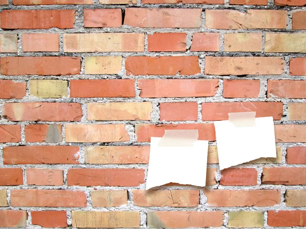 Two pieces of paper with tape on red brick wall