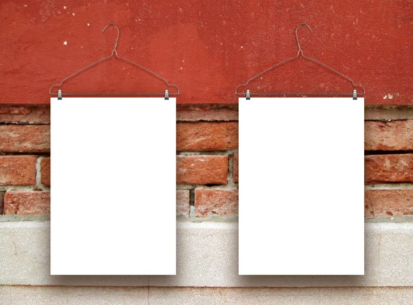 Two vertical paper sheets with clothes hanger on red plastered brick wall