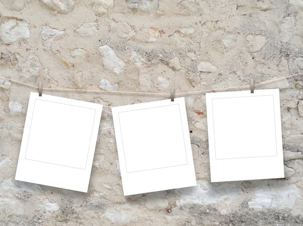Three blank square instant photo frames hung by clothes pin on brown old stone wall