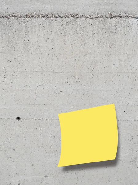 Single yellow square paper sheet on grey concrete wall