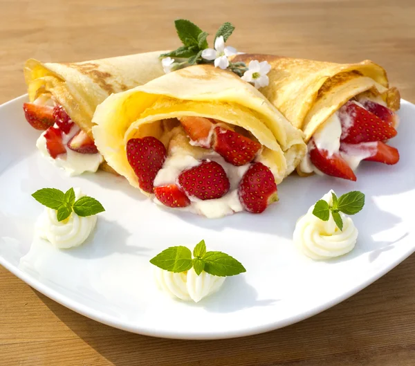 A dessert plate with pancakes, strawberry, whipped cream and mint