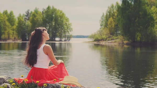 Girl sits on the bank of lake.