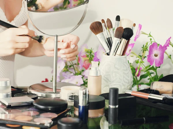 Girl doing makeup Blurred cosmetics foreground.