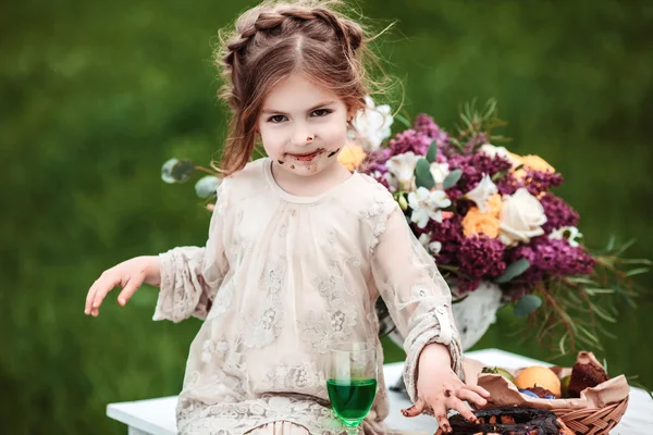 Little baby girl eats chocolate cake in nature at a picnic