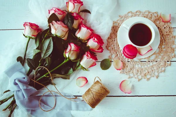 A beautiful bouquet of roses, tea Cup,with macaroons on  distressed white wood table. vintage style