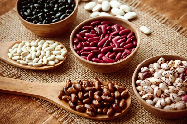 Beautiful multi-colored beans in ceramic bowls on a background of burlap