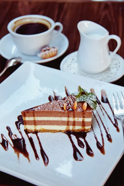 Cheesecake slice with melted chocolate on white plate and coffee