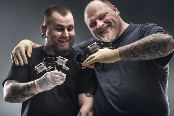 Two men tattoo artists with tattoo machines