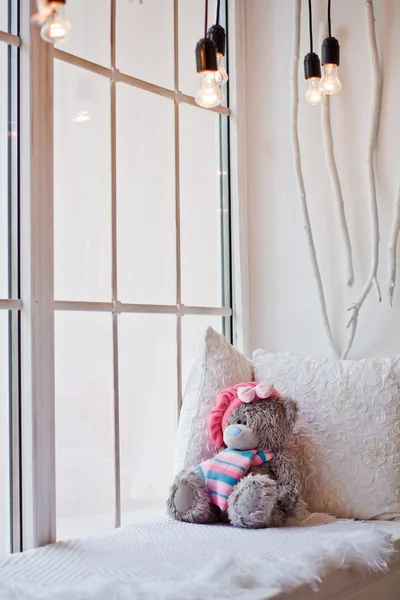 Beautiful Teddy bear sitting on a white bed by the window