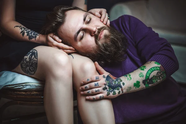 Young couple in love with tattoos, the guy is lying on the lap of the girl