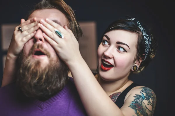 Young couple in love with tattoos having fun, the girl closes hands eyes guy