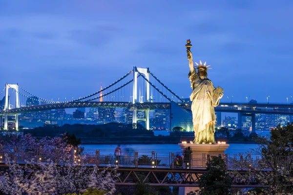 Statue of Liberty and Rainbow bridge, located at Odaiba Tokyo, with Tokyo skyline in background at twilight