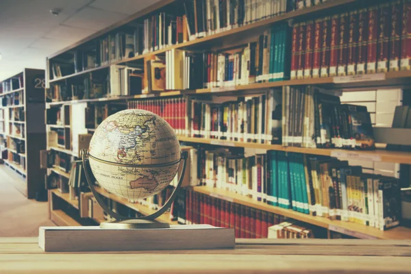 Globe model on textbook, book on old age wood table with blur abstract campus library background