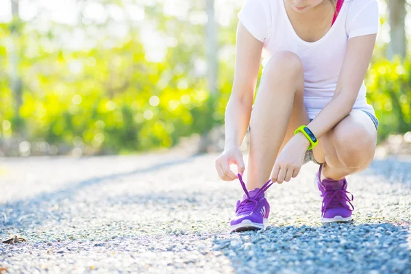 Oung woman in fitness wear tying shoelaces outdoors