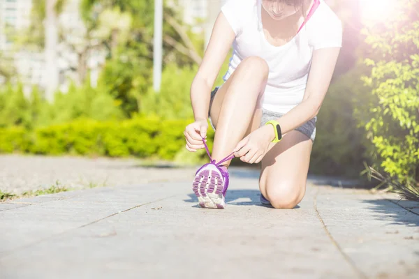 Oung woman in fitness wear tying shoelaces outdoors