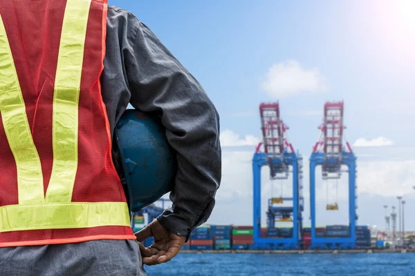 Engineer holding a blue helmet for the safety of workers on the background stock port with cranes and containers