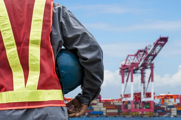 Engineer holding a blue helmet for the safety of workers on the background stock port with cranes and containers
