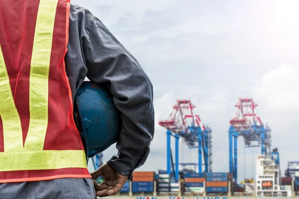 Engineer holding a blue helmet for the safety of workers on the background stock port with cranes and containers