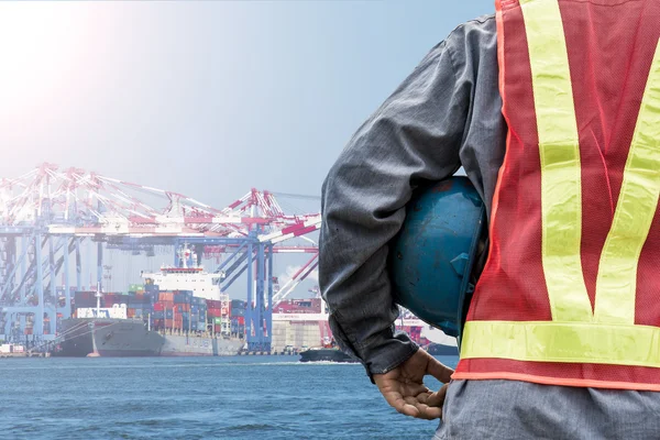 Engineer holding a blue helmet for the safety of workers on the background stock port with cranes and containers