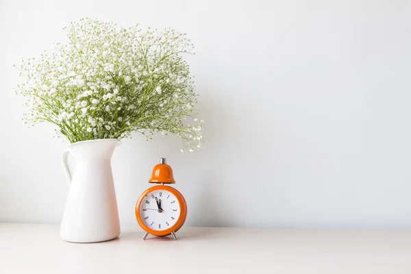 Flowers and  alarm clock on a white wall shelf
