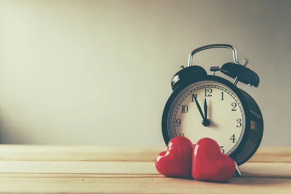 Red alarm clock with couple heart of love on wooden background