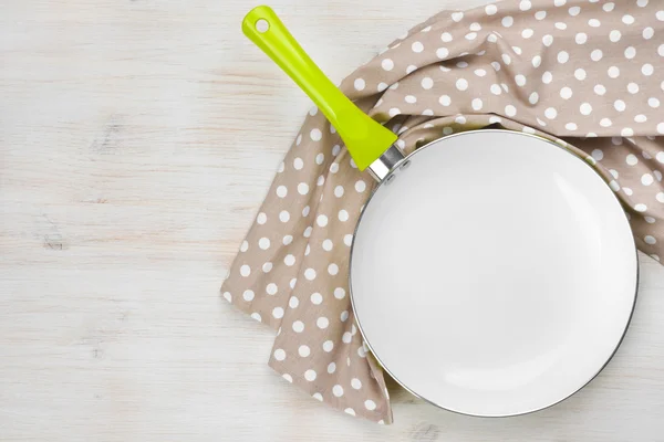 Green handle frying pan and kitchen towel over wooden background