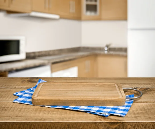 Wooden cutting board, blue checkered towel over blurred kitchen background