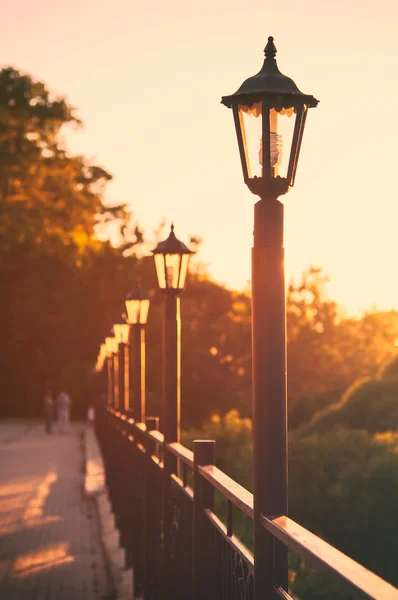 Street lights along the fence, the sun\'s rays.The people in the background.