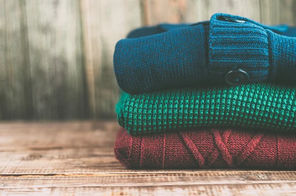 Warm clothes laid in a pile on wooden background.Colorful sweaters on a wooden table.