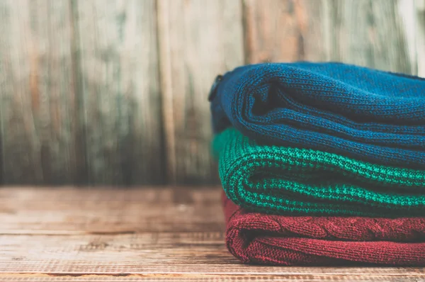 Warm clothes laid in a pile on wooden background.Colorful sweaters on a wooden table.