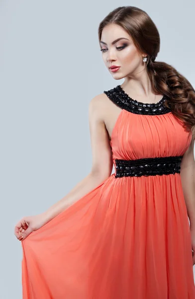 Fashion portrait of young elegant woman in evening coral dress