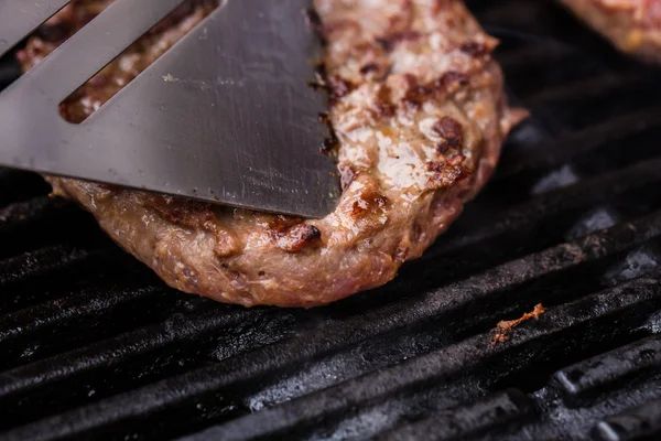 Grilled ground beef pattie burger on spatula against BBQ